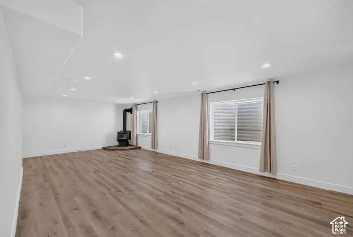 Spacious room featuring wood-finish flooring, recessed lighting, and a freestanding stove with a brick hearth