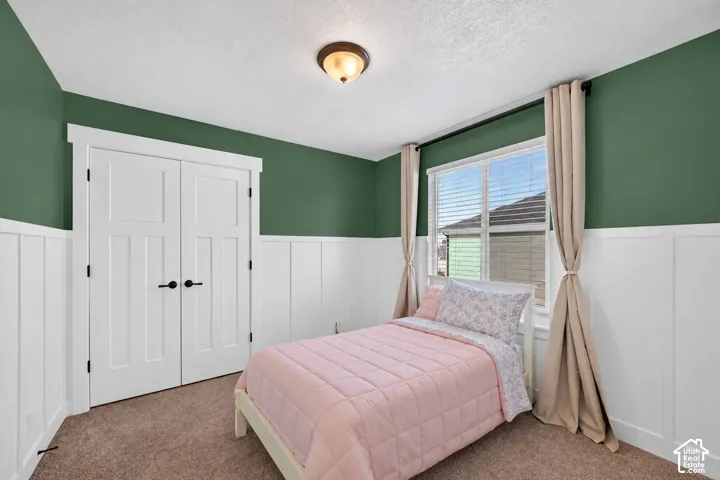 Board and batten wall paneling, large window with blinds, ceiling-mounted light fixture, and textured carpeting