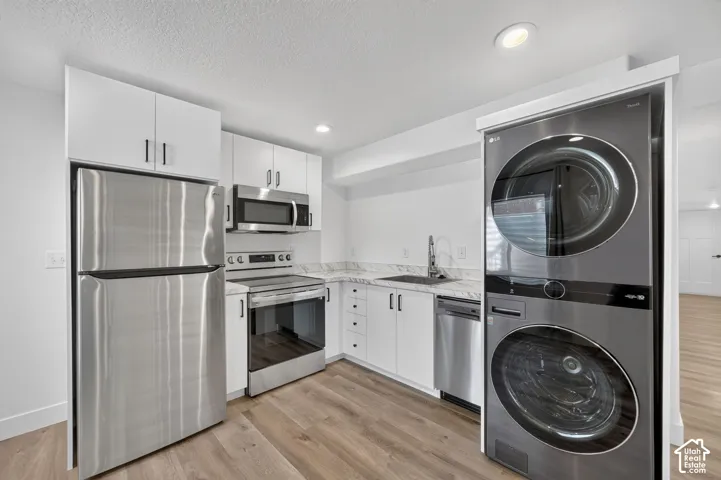 Modern kitchen featuring stainless steel appliances, white cabinetry, wood-finish flooring, and a stacked washer/dryer