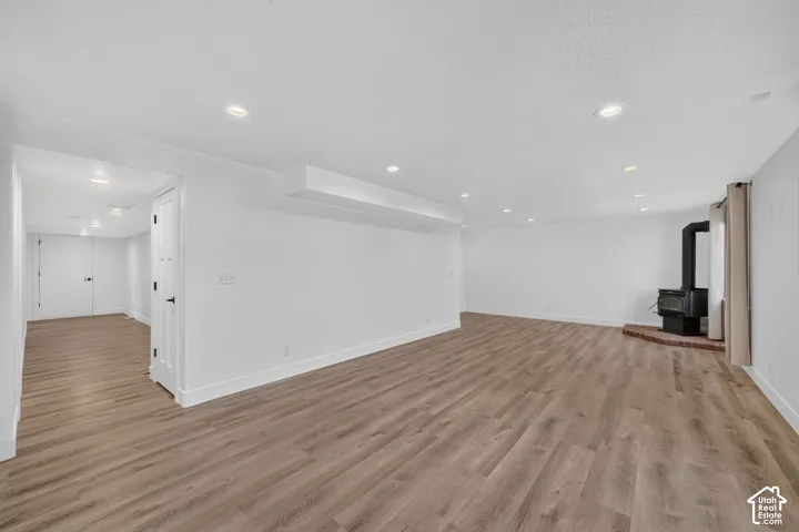 Spacious room featuring wood-finish flooring, recessed lighting, and a black wood-burning stove on a brick hearth