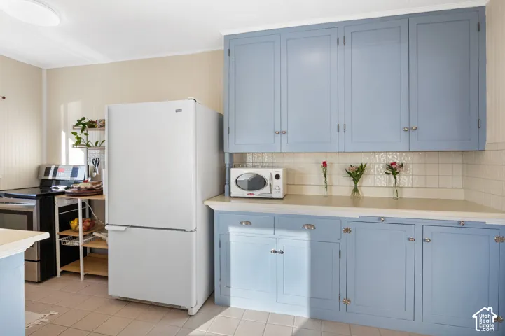 Kitchen with grey blue cabinetry, classic hardware and included refrigerator.
