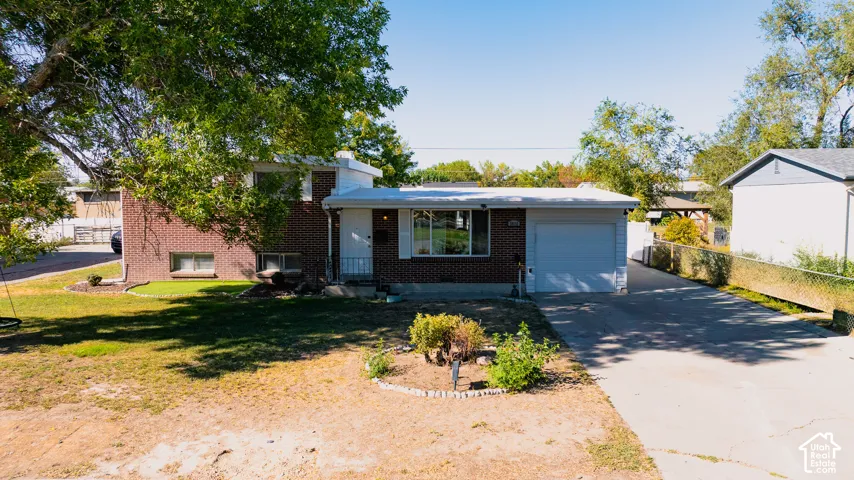 Brick exterior with white trim, attached garage, concrete driveway, and mature trees