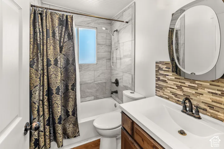 Full bathroom featuring a single vanity with a white countertop, a mosaic tile backsplash, and a tub with a tile surround