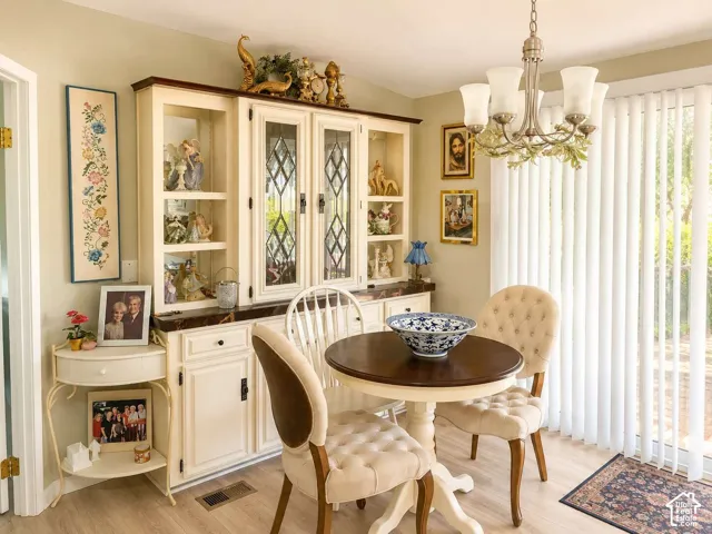 Light wood-finish flooring, decorative chandelier, and vertical blinds