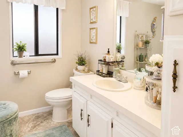 Frosted glass window, white vanity with integrated sink, white cabinetry with bronze hardware, and light-toned flooring