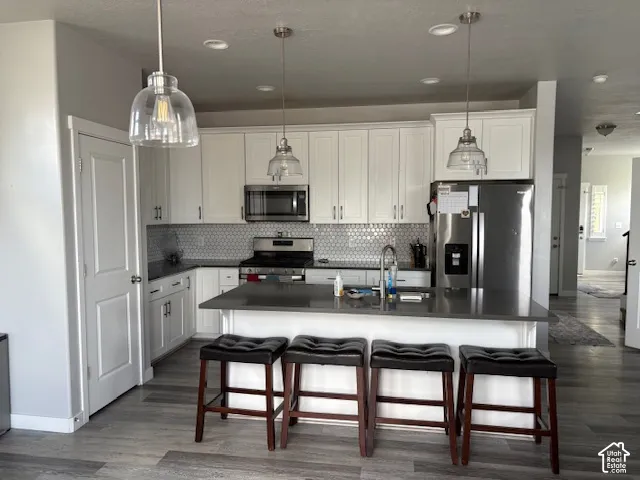 Chef's kitchen featuring white cabinetry, stainless steel appliances, gray subway tile backsplash, and a large center island with seating for four