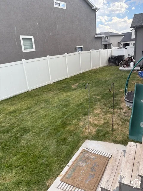 Expansive backyard featuring a green lawn, white privacy fencing, and a concrete patio