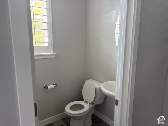 Compact powder room featuring a standard toilet, pedestal sink, and horizontal window with louvered shutters allowing natural light