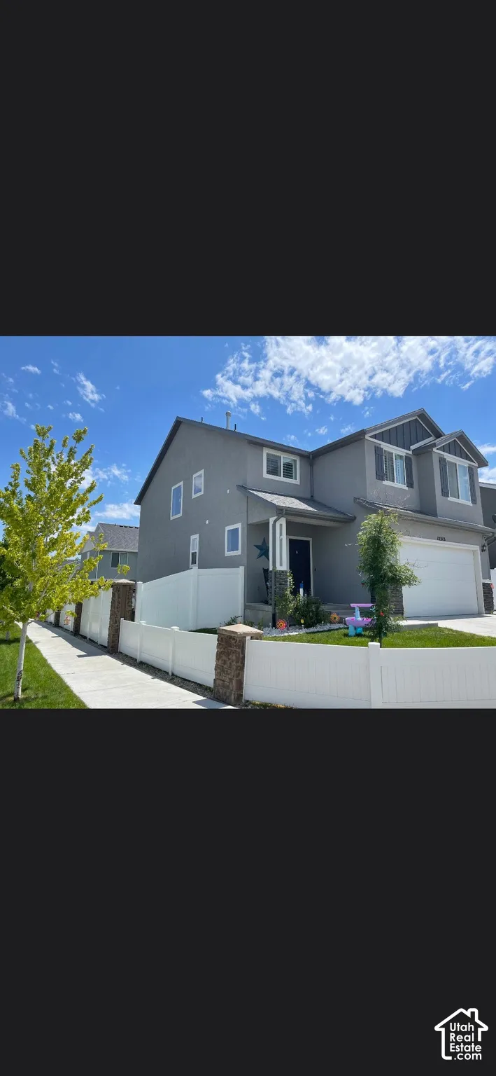 Two-story exterior featuring grey siding, stone accents, white vinyl fencing with stone pillars, and an attached two-car garage