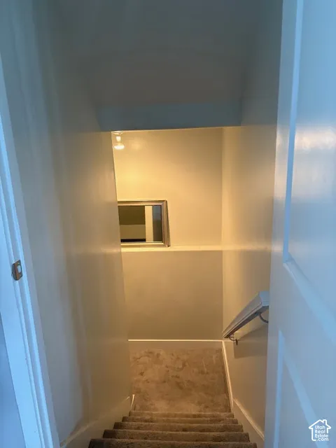 Carpeted staircase with white trim, a fixed wall-mounted railing, and a small built-in window