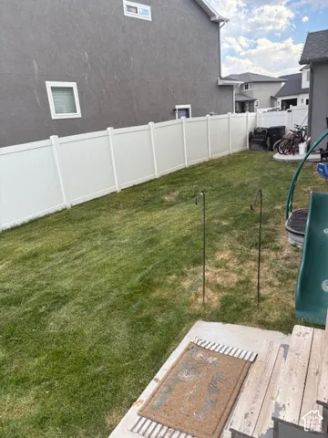 Expansive backyard featuring a manicured lawn, a solid white privacy fence, and a concrete patio with wood-finish steps