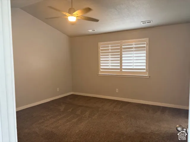 Vaulted ceiling with ceiling fan, white plantation shutters, and textured carpeting