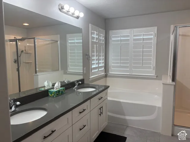 Dual vanity with integrated sinks and dark countertops, white cabinetry with dark hardware, built-in bathtub, and a glass-enclosed shower