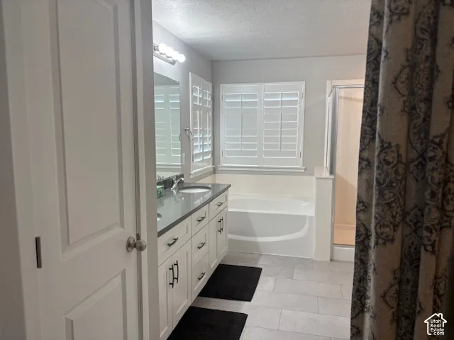 Double vanity with dark countertops, white cabinetry with dark hardware, built-in bathtub, and a shower enclosure