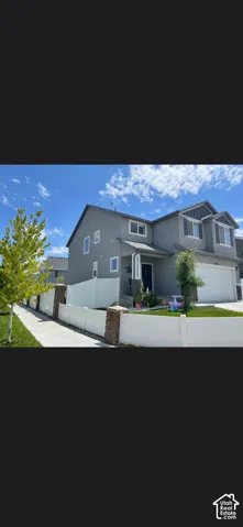 Two-story exterior featuring grey siding, stone accents, white vinyl fencing with stone pillars, and an attached two-car garage
