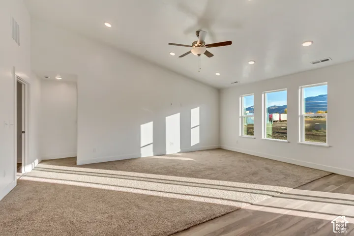Spacious primary suite bathed in natural light through multiple windows, featuring neutral wall finishes, recessed ceiling lighting, and a ceiling fan with brushed metal accents