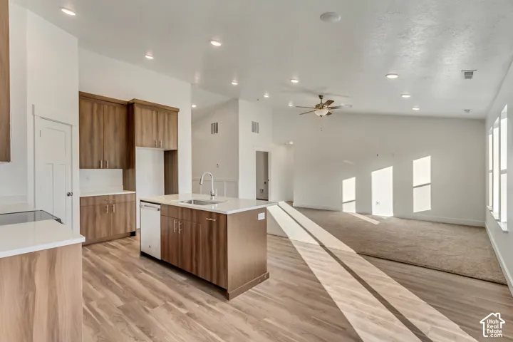 Open-concept kitchen featuring wood-finish cabinetry, white countertops, and a center island with an undermount sink