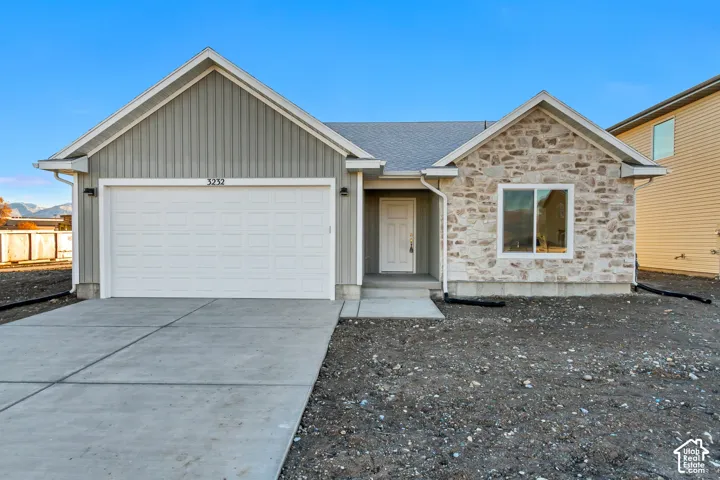 Modern ranch home featuring a striking brick and stone exterior, two-car garage with white paneled door, and a freshly poured concrete driveway