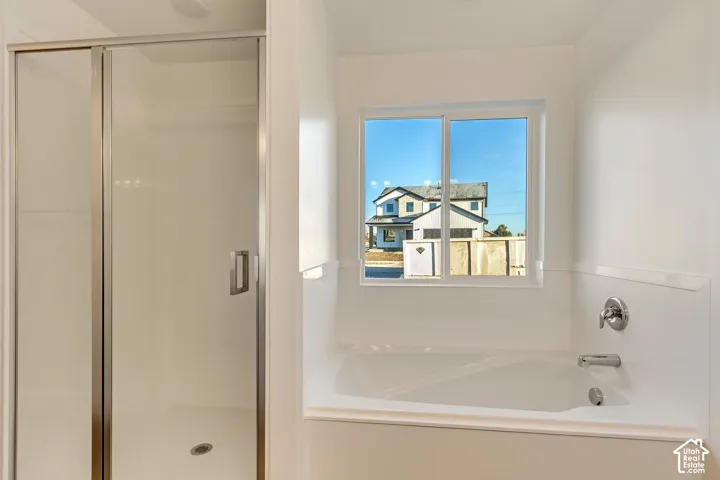 White soaking tub with chrome fixtures, an adjacent shower with a clear glass enclosure, and a window providing natural light