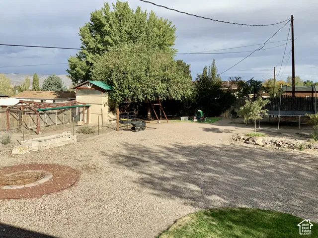 Expansive gravel yard featuring a built-in fire pit, mature trees, and a dedicated garden structure with a green roof