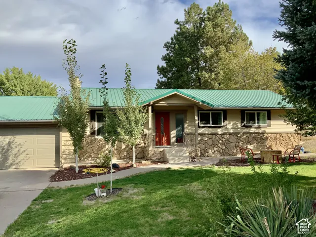 Green metal roof, tan siding, stone facade, covered entry, and attached garage