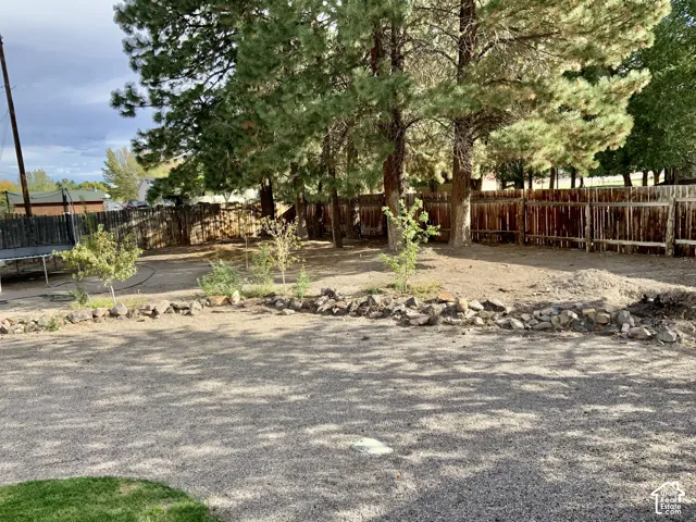 Spacious outdoor area featuring established trees, a wood privacy fence, and a gravel surface