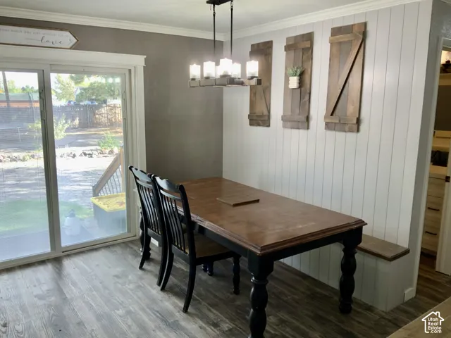 Dining area featuring wood-finish flooring, shiplap accent wall with three framed architectural prints, pendant lighting fixture, and sliding glass doors overlooking the outdoor space