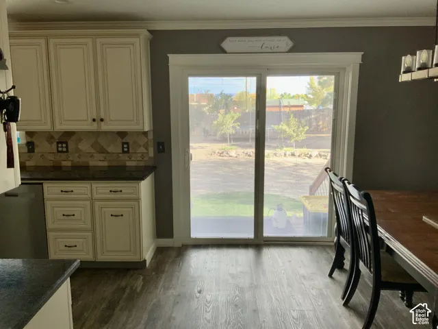 Wood-finish flooring, cream cabinetry with dark hardware, dark countertops, and a decorative tile backsplash