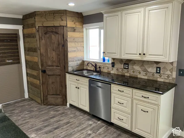 Cream-colored cabinetry with dark hardware, dark countertops, patterned tile backsplash, stainless steel sink with coordinating faucet, and wood-finish flooring