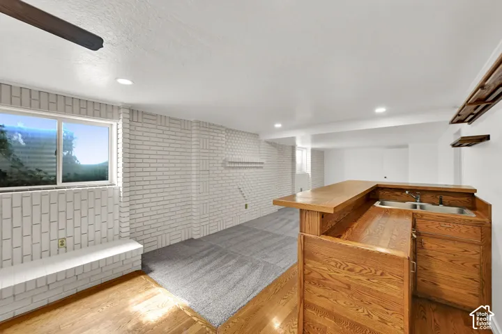 Wood-finish flooring, recessed lighting, white painted brick walls, built-in window bench, and an integrated wet bar with a double sink