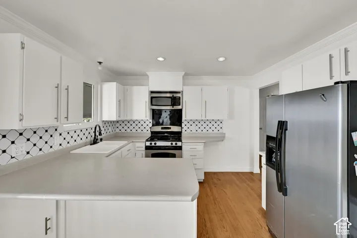 White cabinetry with brushed nickel hardware, light-toned countertops, black and white geometric tile backsplash, stainless steel appliances, and wood-finish flooring