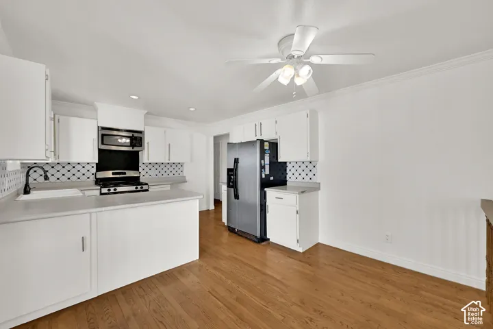 White cabinetry with stainless steel appliances, wood-finish flooring, and a decorative tile backsplash