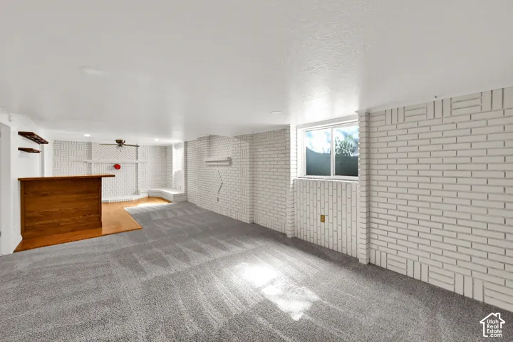 Spacious room featuring light-colored carpeting, white brick wall accents, and a built-in wood-finish bar