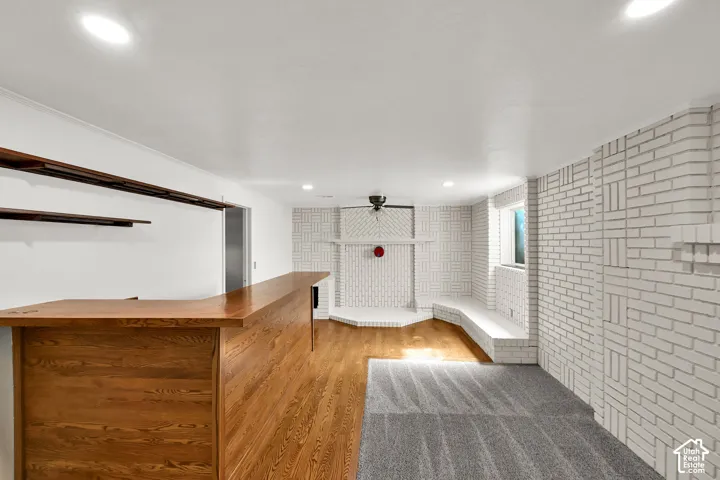 Built-in wood-finish bar with shelving, wood-finish flooring, recessed lighting, and white painted brickwork with integrated seating