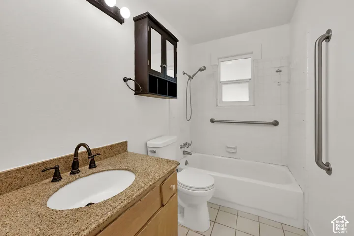 Vanity with granite-style countertop, bronze-finish faucet, built-in medicine cabinet, white tiled shower, and white ceramic tile flooring