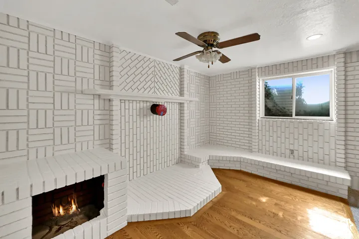Brick wall finishes, built-in brick seating, fireplace with hearth, wood-finish flooring, and a ceiling fan with integrated lighting