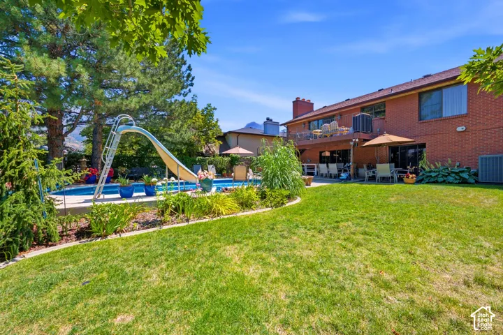 Expansive backyard featuring a swimming pool with slide, brick exterior, upper-level deck, and established landscaping