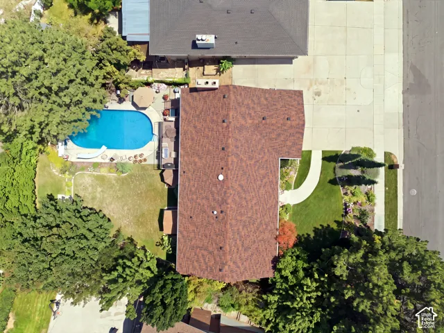 Oval-shaped swimming pool, paved pool deck, surrounding green landscaping, mature trees, and a paved driveway