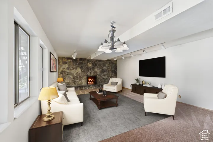 Stone-clad fireplace feature wall, multiple windows, recessed ceiling lighting, track lighting, and a decorative chandelier