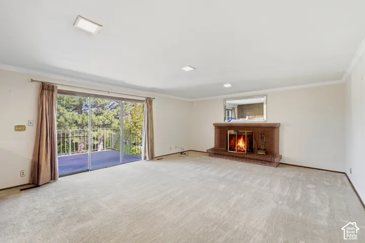 Spacious room featuring a brick fireplace with a mantel, crown molding, recessed lighting, and sliding glass doors opening to an outdoor balcony