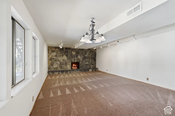 Stone fireplace with hearth, multiple windows, decorative chandelier, and track lighting
