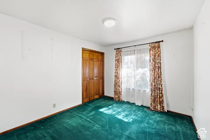 Window with white sheer curtains, wood-finish bi-fold closet doors, green carpet, and a flush mount ceiling light
