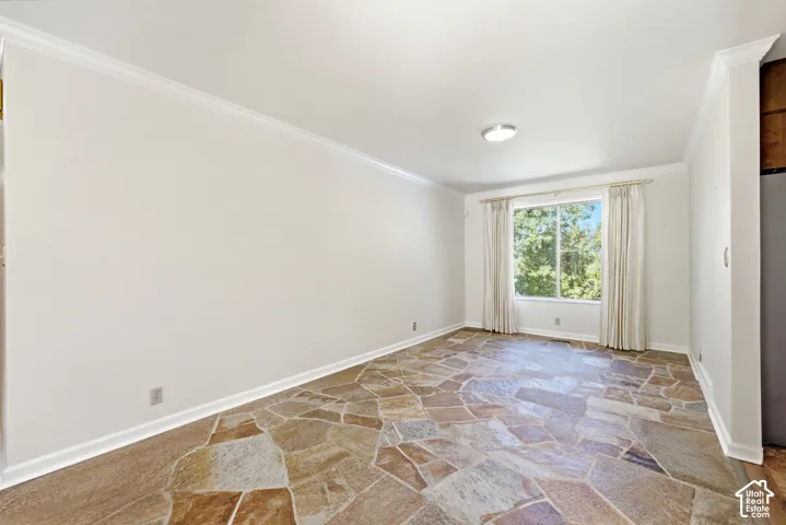Room featuring natural stone flooring, a large window, a flush-mount ceiling light, white crown molding, and white baseboards
