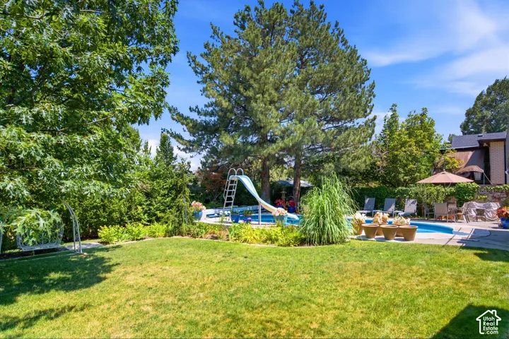 Expansive backyard featuring a manicured lawn, a built-in swimming pool with a slide, and mature trees