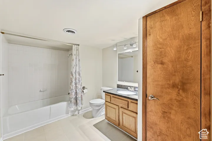 Bathroom featuring a white bathtub with tile surround, wood-finish vanity with a single sink, and track lighting