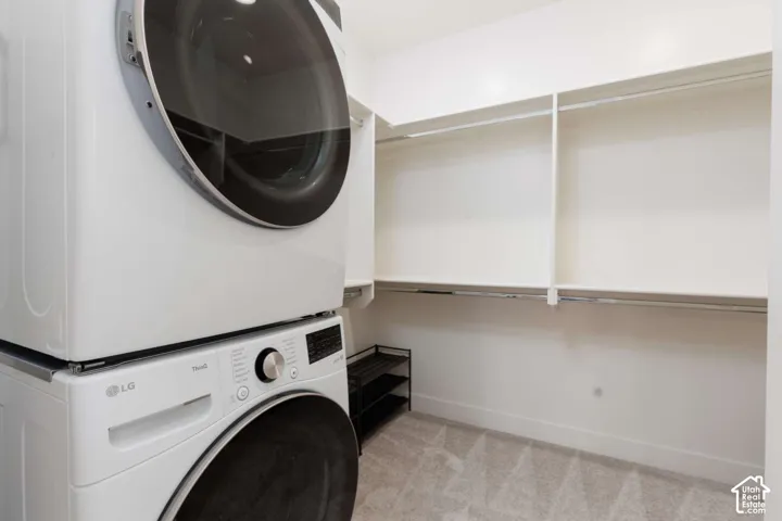 Built-in white shelving and hanging rods, carpeted flooring, and a stacked washer and dryer unit