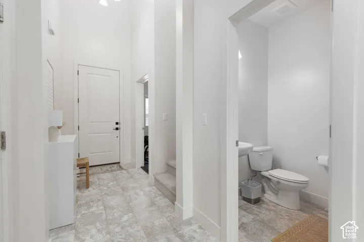 Entryway featuring high ceilings, light-toned tile flooring, a white paneled door with matte black hardware, and an adjacent powder room with a pedestal sink