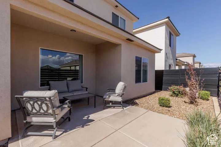 Covered patio with concrete flooring, stucco exterior, and adjacent xeriscaping with a privacy fence