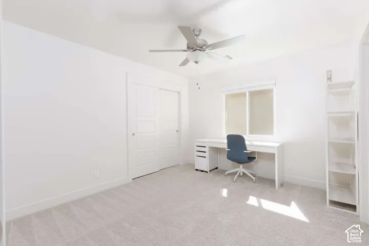Neutral-toned carpeting, ceiling fan with light fixture, window with roller shades, and a sliding two-panel closet door