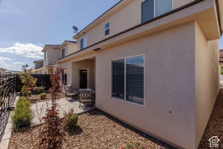 Paved patio area, stucco exterior, multiple windows with blinds, gravel landscaping, and established plantings